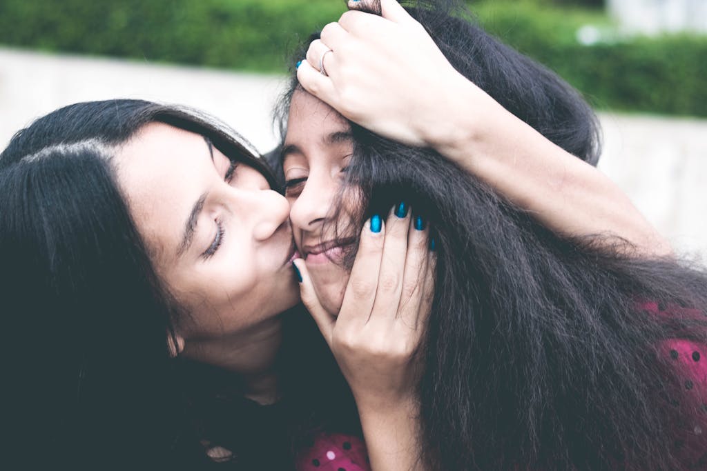 Woman Kissing Cheek of Girl Wearing Red and Black Polka-dot Top